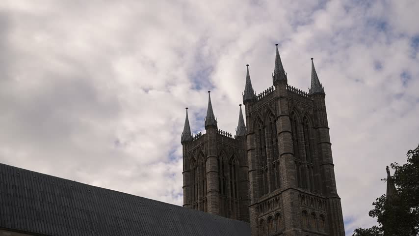 Twin towers of Lincoln Cathedral rise against a shifting cloudy sky in a static low angle side view.