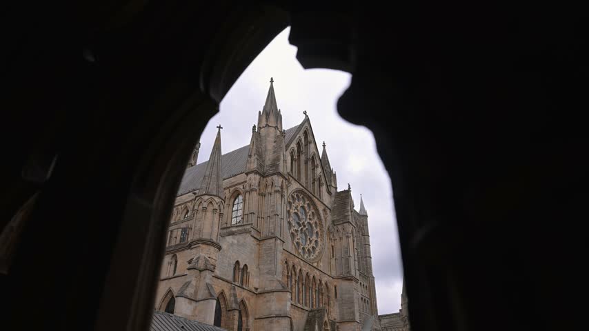 Lincoln Cathedral’s ornate Gothic facade and rose window appear through a dark archway silhouette on a grey day.