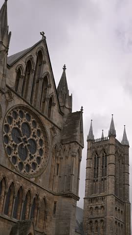 Gothic west front of Lincoln Cathedral with rose window and twin towers framed in a vertical tilt under an overcast sky.