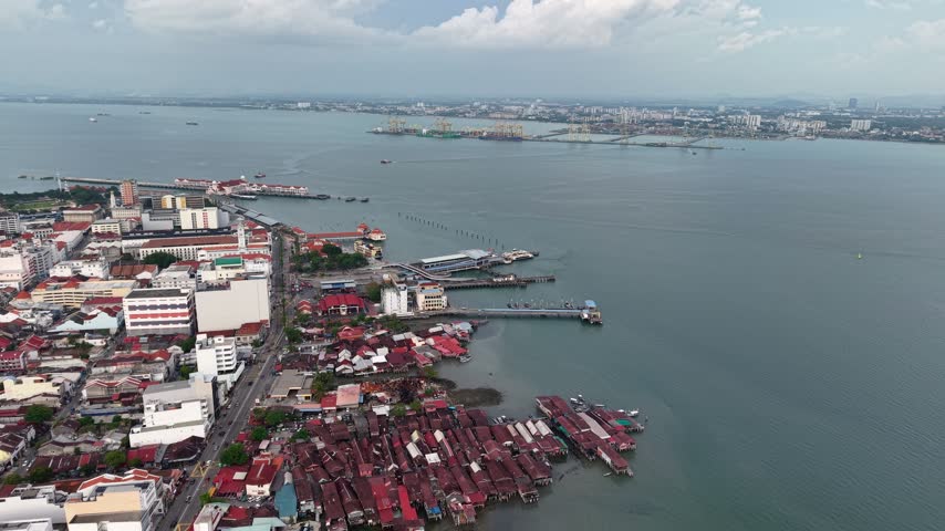 Drone aerial panorama of George Town, Penang, with historic waterfront buildings, clan jetties, harbor traffic, and container port.