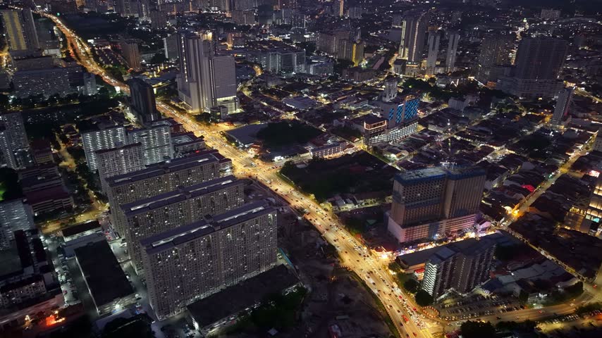 Illuminated George Town cityscape with high-rise buildings, busy roads, and dense urban neighborhoods across Penang at night.