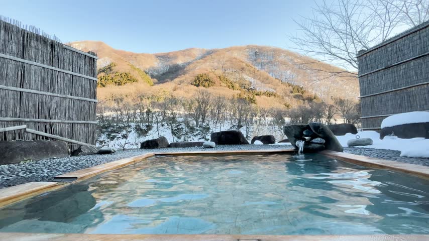 Scenic view of an outdoor hot spring rotenburo with snow-covered mountains under a clear blue sky in Japan.