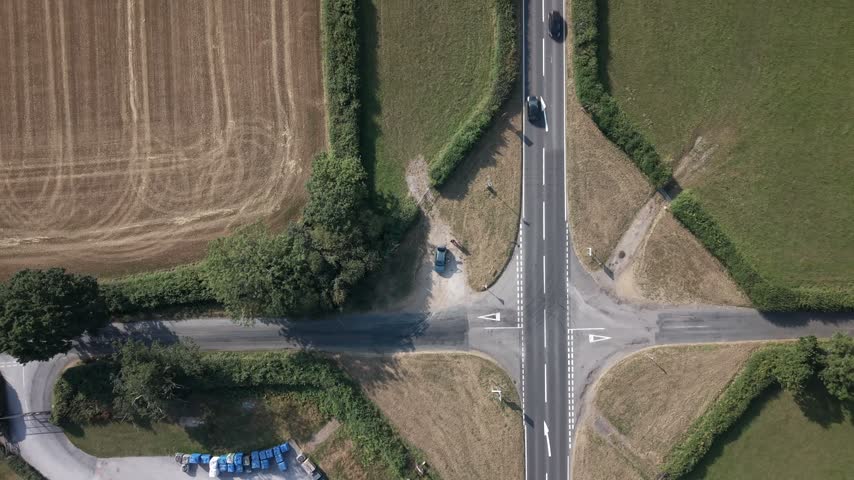 Top-down aerial view of rural crossroads surrounded by harvested fields, green pastures and hedgerows.