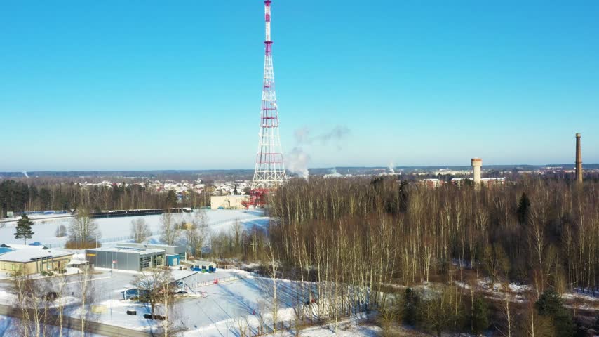 Tall red and white telecommunication tower standing in a winter landscape near a small town