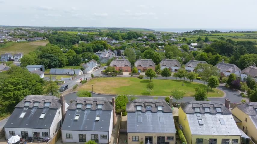 Central lawn, thatch-style homes, and surrounding Irish countryside unfold as the camera glides above St James Wood estate.