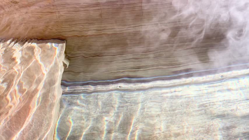 Hot spring water pouring into a wooden bathtub with rising steam in Japan.