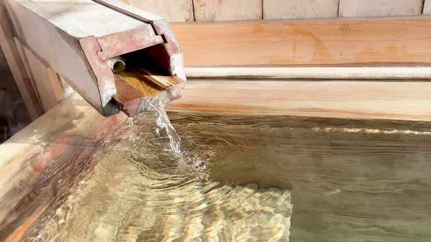 Hot spring water pouring from a wooden spout into a wooden bath tub in Japan.