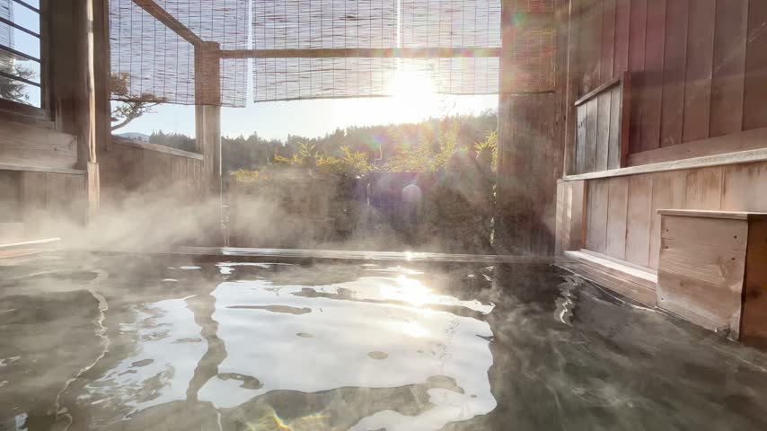 Scenic view of a traditional Japanese wooden open-air hot spring rotenburo with rising steam and warm sunlight in Japan.