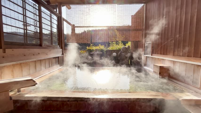 Scenic view of a traditional Japanese wooden open-air hot spring rotenburo with rising steam and warm sunlight in Japan.