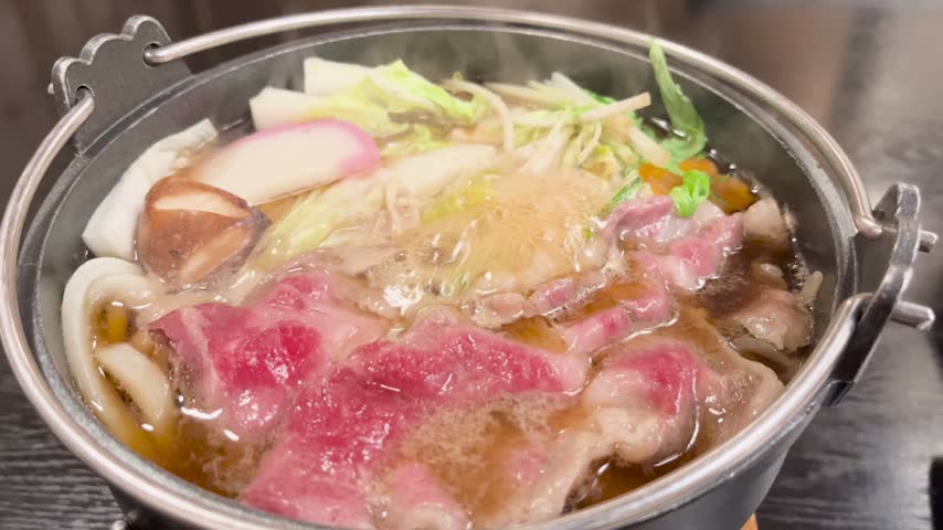 Traditional Japanese gourmet hot pot dish simmering with sliced beef, vegetables, and noodles in a pot in Japan.