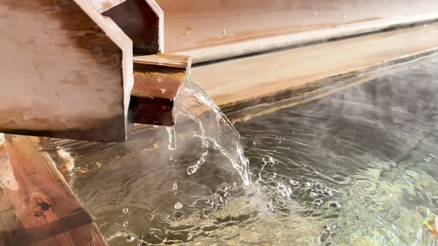Hot spring water pouring from a wooden spout into a wooden bath tub in Japan.