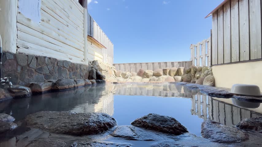 Scenic view of an open-air rock hot spring rotenburo reflecting the blue sky and surroundings in Japan.