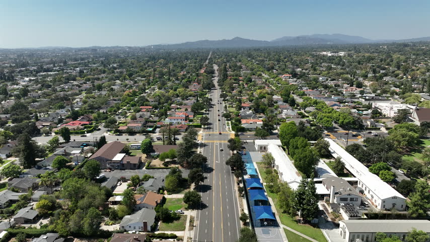Pasadena, California, USA - Aerial view of Orange Grove Boulevard passing through a quiet residential neighborhood with homes and scenic hills in the background on a bright day.