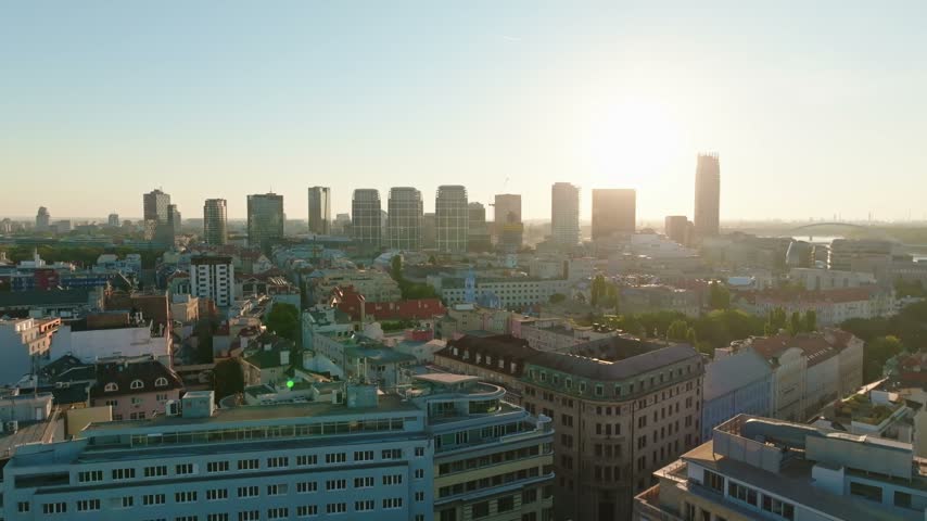 Aerial panorama of Bratislava in Slovakia with residential rooftops below modern towers and a bright low sun illuminating the urban horizon