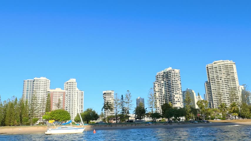 Sunny waterfront view of high-rise apartment buildings and a moored sailboat on the Gold Coast.
