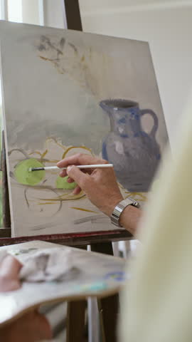 Vertical shot of artist painting still life with brush on canvas from over shoulder. Footage suitable for retirement lifestyle and creative hobby campaigns