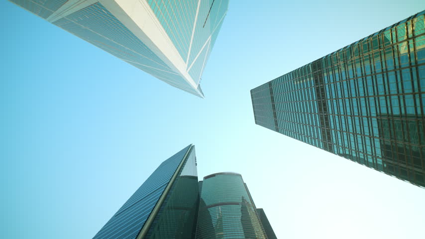 Low angle view looking straight up at glass skyscrapers in central Hong Kong against a clear blue sky as the camera slowly rotates. Modern business district architecture.