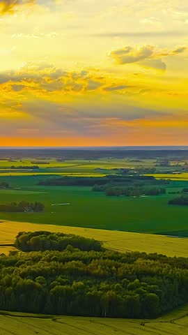 Dramatic sunset clouds move over wide green and yellow farmland in rural landscape