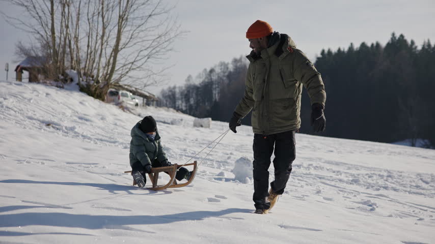 Smiling African American father pulls his young son on a wooden sled, enjoying quality time together and playful winter fun in the snow.