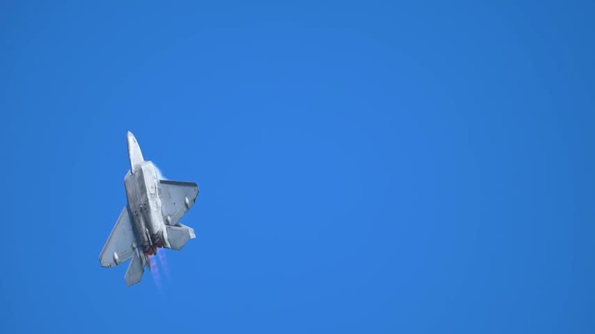 An F-22 Raptor Stealth Fighter Jet Soars High Across A Cloudless Clear Blue Sky.