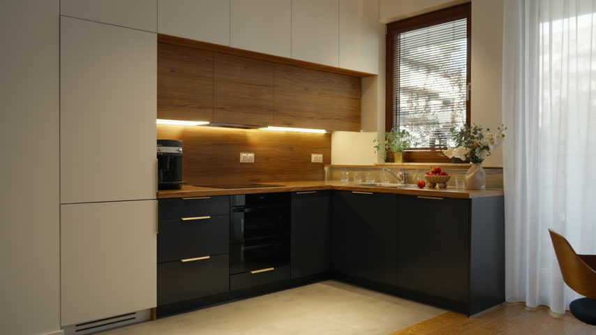 Bespoke kitchen cabinetry with tall storage units, wooden cupboards, and built-in appliances stands in a modern apartment. Open layout connects the furniture set with a dining table.