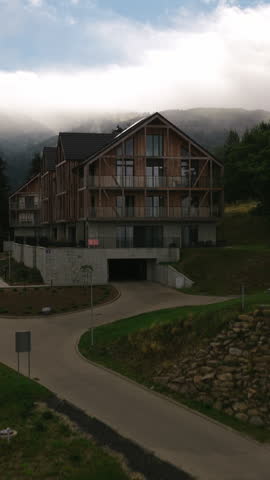 Exterior View Of Modern Alpine Hotel Chalet With Wooden Facade And Large Windows With Mountain Landscape Of Karkonosze In The Background. - aerial vertical shot