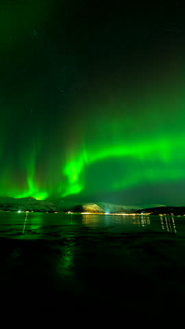 Vivid green aurora borealis swirling above a snow-covered mountain and starry sky at Bentsjord, Tromsø, Troms, northern Norway, vertical timelapse
