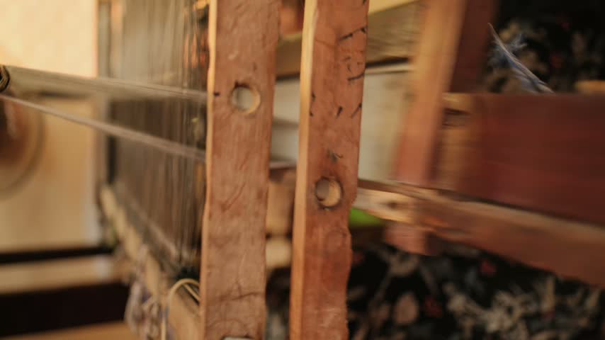 Close view of wooden loom uprights, warp threads and patterned cloth in Chau Phong, Vietnam, accompanied by the recorded sound of the loom.