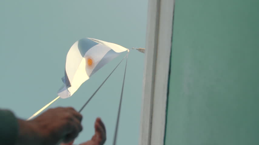 Hand hoisting a small Argentine flag outdoors in Argentina.
