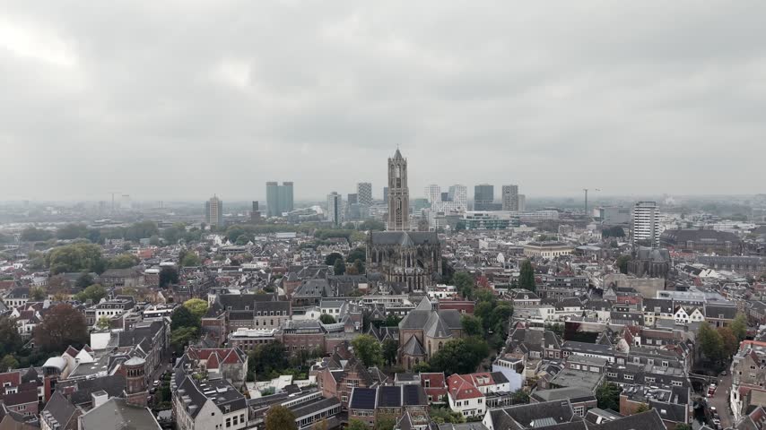 Aerial view across Utrecht rooftops toward the prominent Dom Tower and distant city skyline on a grey cloudy day in the Netherlands, 4K.