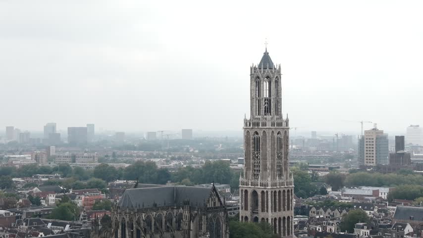 Close aerial view of the Gothic Dom Tower in Utrecht standing above green trees, historic streets and the distant city skyline, 4K.