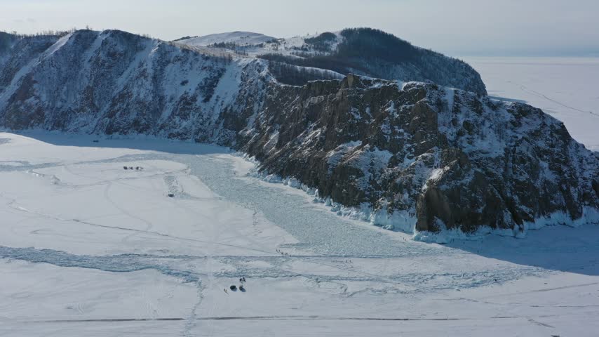 Aerial view of the frozen expanse of Lake Baikal with snow-covered cliffs and ice formations under a clear sky in Russia.