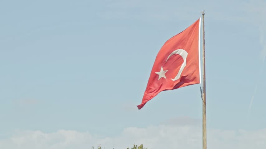 Turkey, Istanbul 2023 09 20: A Turkish flag waving proudly on a flagpole against a clear blue sky, medium shot perspective with distant city buildings.