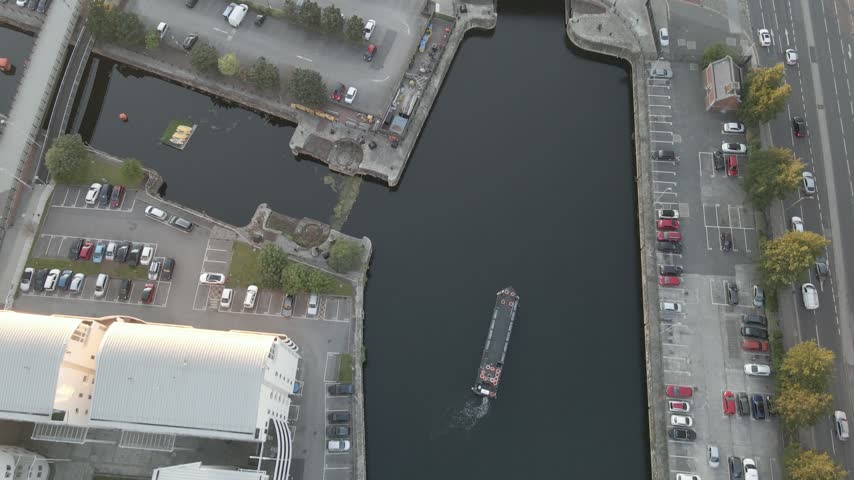 Overhead view of a boat travelling through a dock basin beside waterfront buildings in Liverpool, England, United Kingdom.