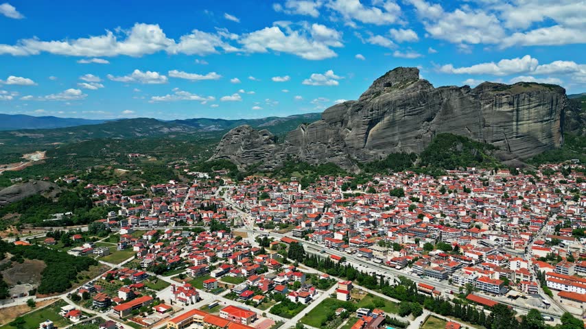 Aerial view of the historic town of Trikala nestled beneath the dramatic rock formations of Meteora with red-tiled rooftops and lush green surroundings in Trikala, Greece.