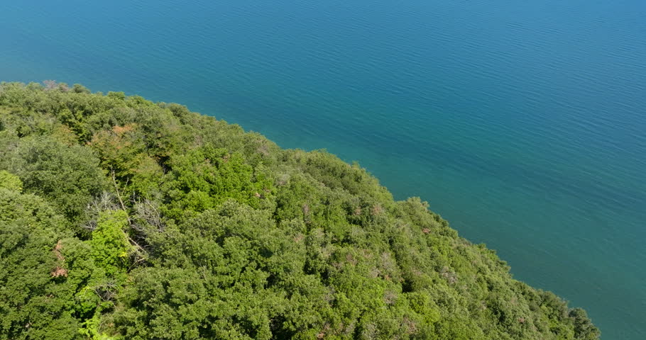 Aerial view of a green wooded hillside sloping down to the deep blue water of a lake on a sunny summer morning.