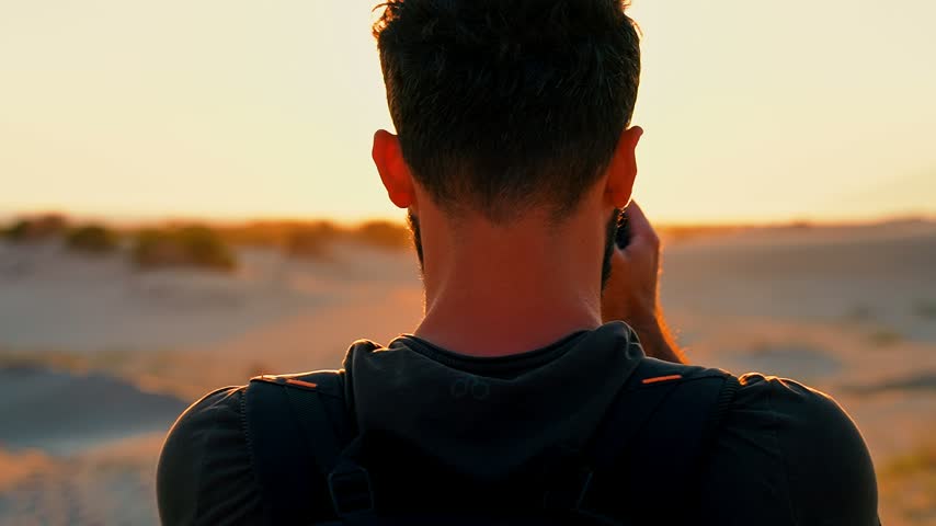 Close-up of a photographer capturing the sunset with a camera on the beach. Warm golden light highlights the moment in a striking coastal setting.