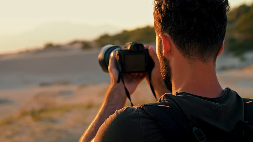 Close-up of a photographer capturing the sunset with a camera on the beach. Warm golden light highlights the moment in a striking coastal setting.