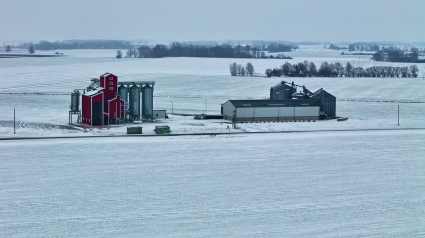 Aerial view of a farm with red buildings and silos in a snowy landscape in Jelgava, Latvia.