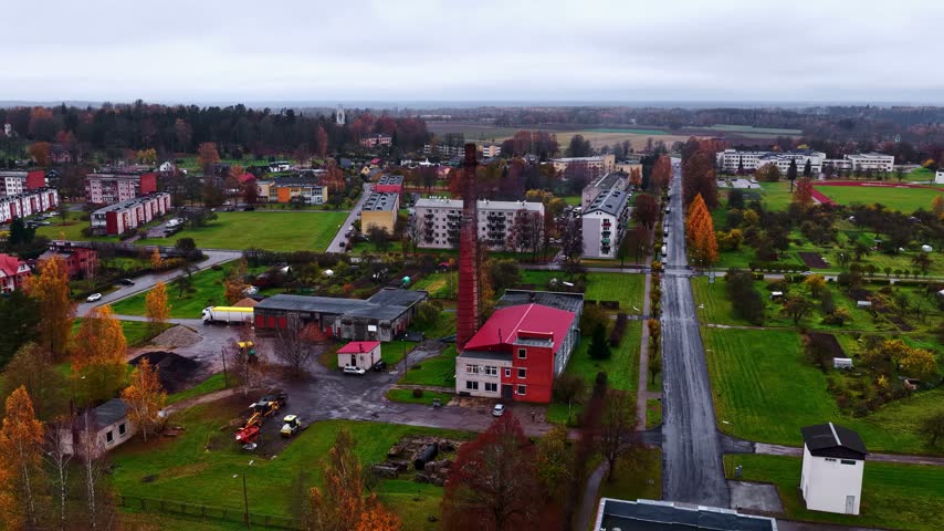 Aerial view of the town of Priekuli with its prominent brick chimney, surrounding residential buildings, and autumn foliage in Priekuli, Cesis Municipality, Latvia.