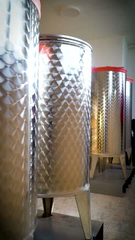 Upright stainless steel barrels with legs are lined up on a metal shelf in a distillery.
