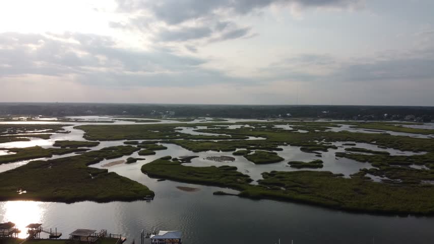 Aerial drone shot of a vast green salt marsh cut by winding tidal channels reflecting the evening sky near Murrells Inlet, South Carolina, USA.
