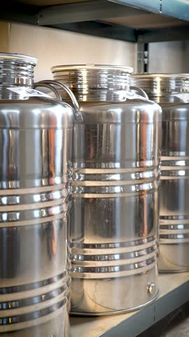 Stainless steel barrels are lined up on a metal shelf in a spirits distillery.