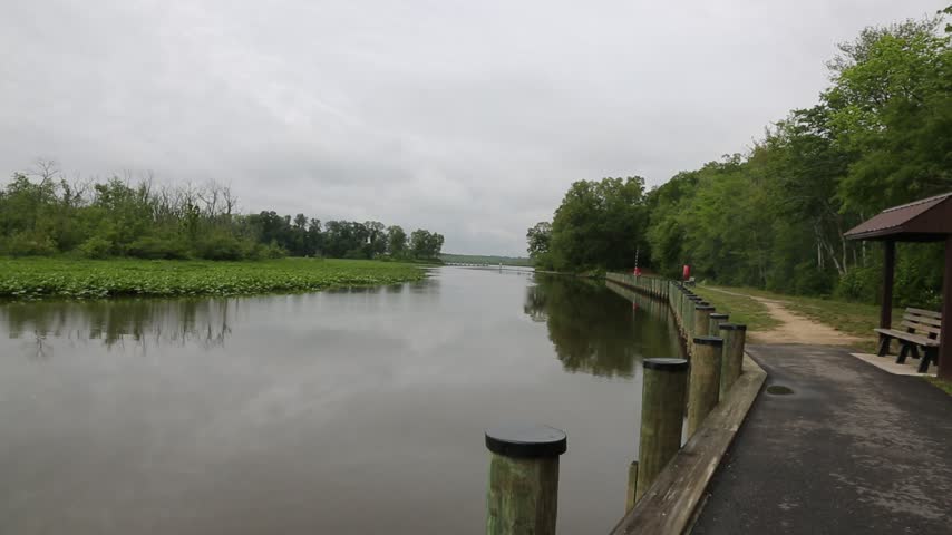 Wooden waterfront boardwalk with pilings and a gazebo beside a calm tidal river and marsh on an overcast spring day, Maryland, USA.
