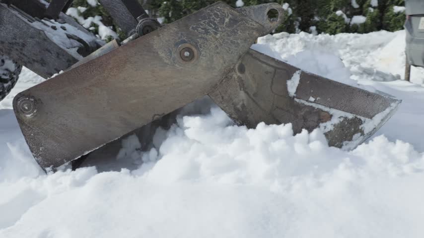 Close side view of a metal snowplow attachment cutting into a thick snowbank and pushing fresh snow during mechanical yard clearance.