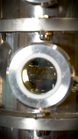 In a close-up shot of distillation taking place in a column still at a distillery, the dance of alcohol droplets can be seen through a round window.