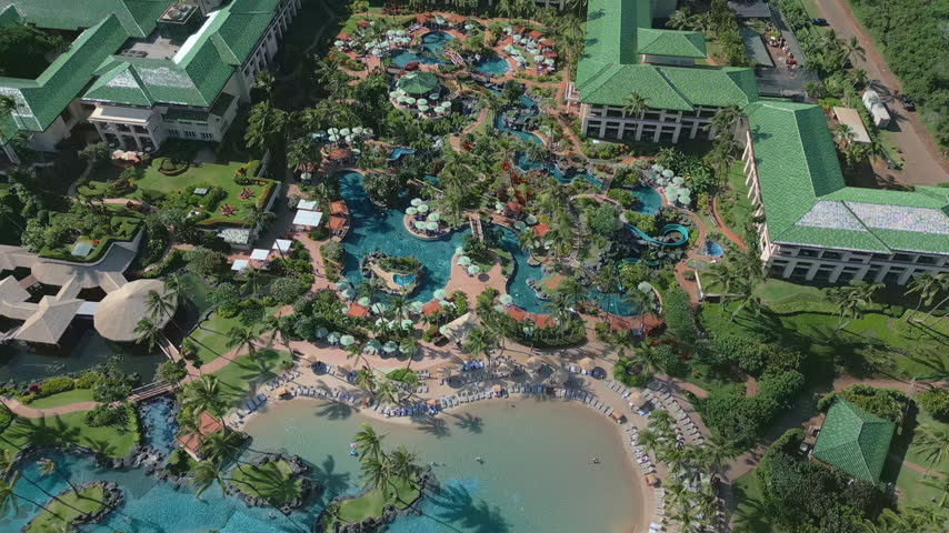 An aerial view reveals resort pools and colorful waterslides among palm trees.