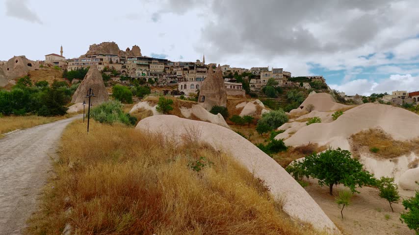 Pathway leads through rocky landscape toward Uchisar town under cloudy sky