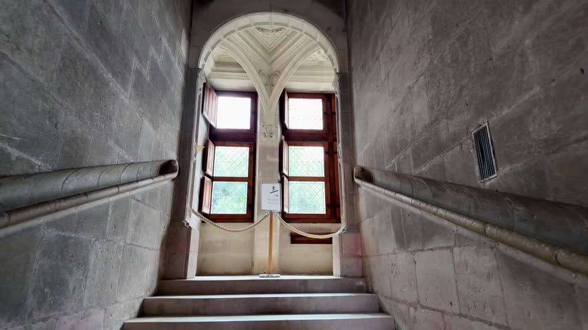 Historic staircase inside Azay-le-Rideau Chateau near Tours, with carved stone arches and symmetrical walls.