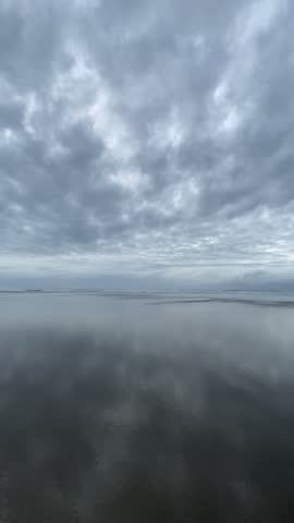 Calm sea waves on a wide sandy beach reflecting overcast sky and clouds at dusk